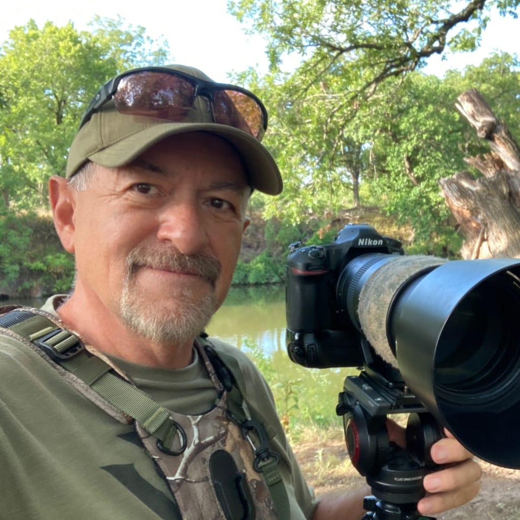About Martin Perea poses next to a river with his camera