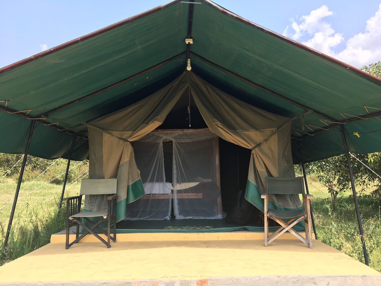 img 0302 Canvas safari tent at Fisi Camp with two chairs on the front porch, mosquito netting visible over the bed inside, surrounded by open grass and trees.